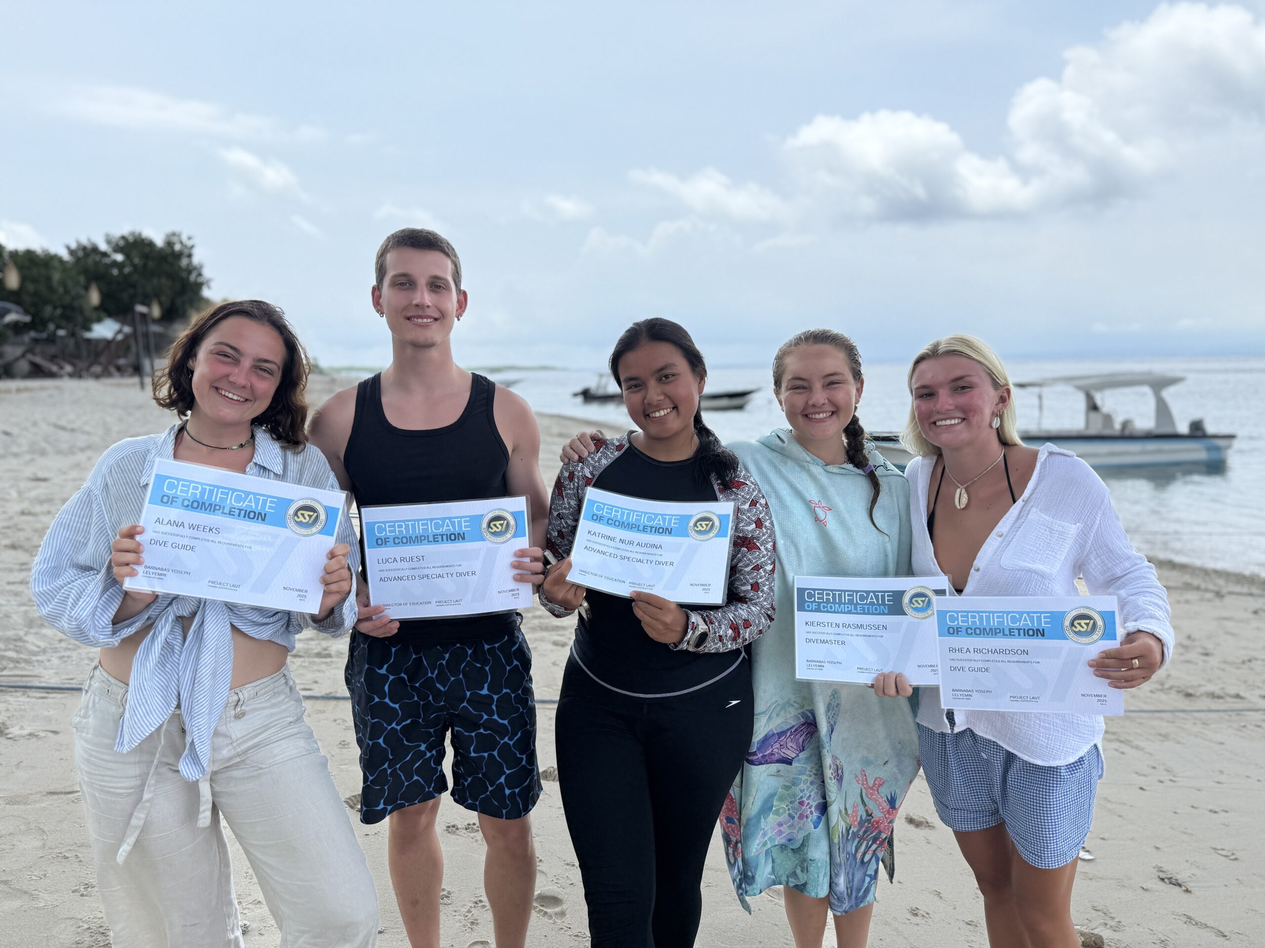 About Project Laut team members standing on the beach in Nusa Penida smiling and holding dive certifications.

